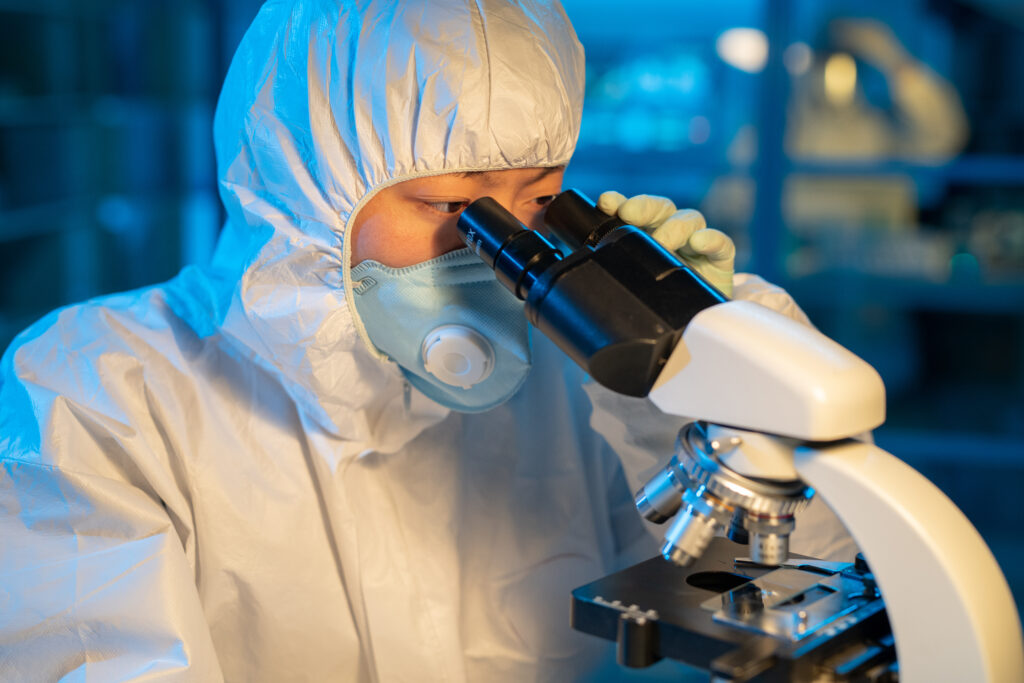 Young female virologist studying new virus in microscope in laboratory